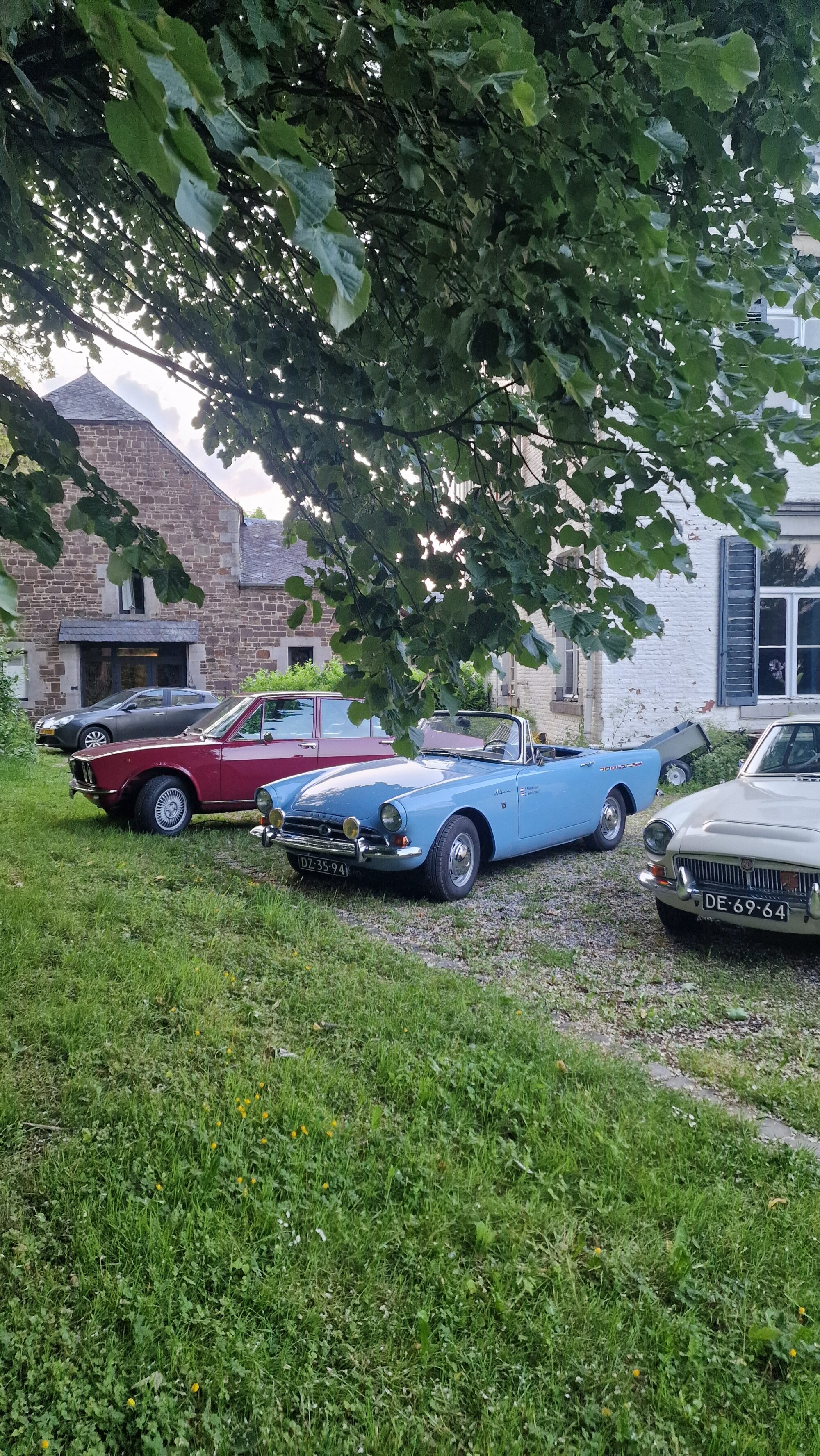 Classic Cars Exhibition at Blier Castle, with three cars, one red, one blue and one white, under a tree.