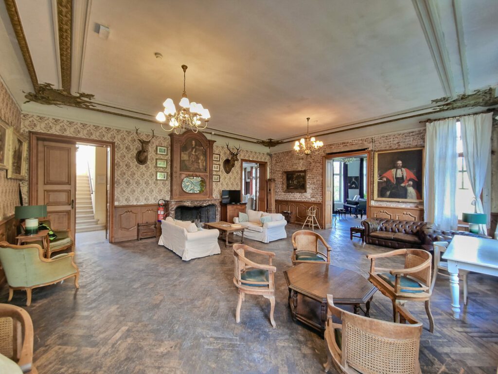 De woonkamer van het Château de Blier, met banken, fauteuils en antieke meubels op een parketvloer voor een gezellige en ontspannen sfeer.

