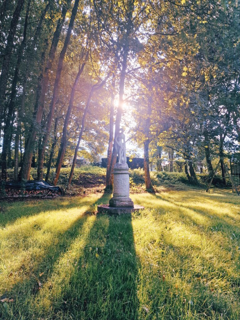 Découvrez le Château de Blier 3 Vue verticale de la statue dans le jardin du château de Blier, sous les arbres et avec le soleil en arrière-plan.